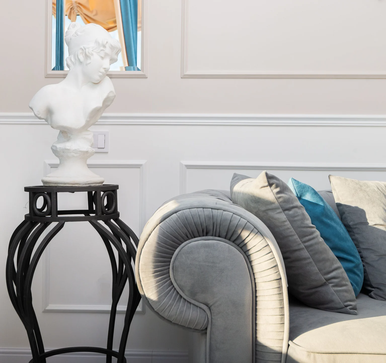 Modern living room interior with decorative sculpture on pedestal against couch with cushions in sunlight